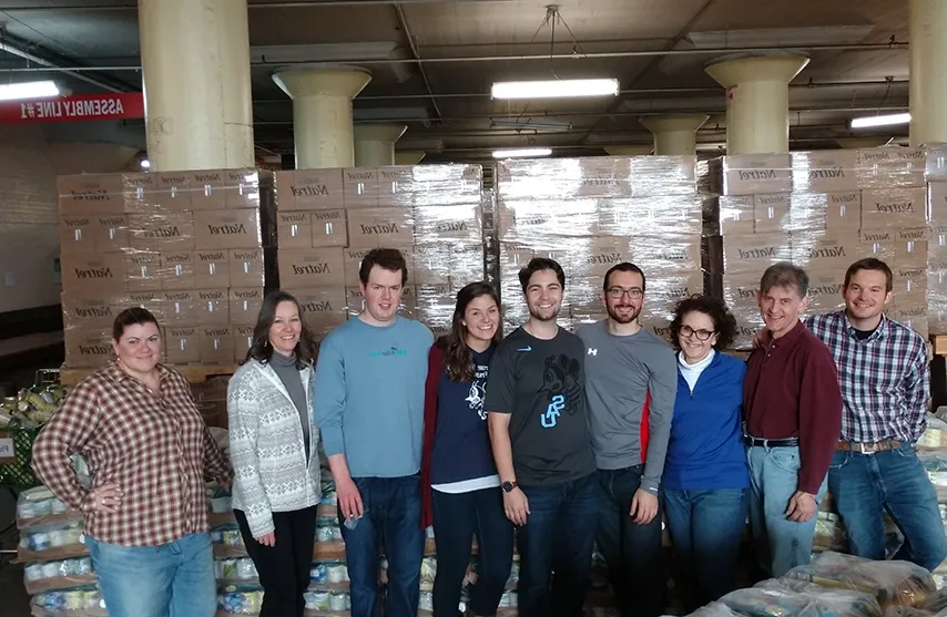 A group of volunteers stand in front of boxes of donated food.